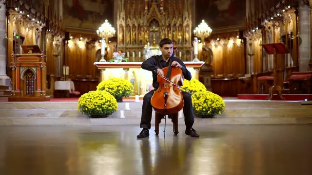 alone adult musician is sitting on a chair in center of church hall and playing cello, contemporary concert
