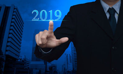 Fototapeta na wymiar Businessman pressing 2019 text over modern office city tower and skyscraper, Happy new year 2019 calendar cover concept