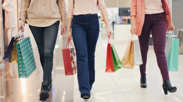 Low shot of ladies' legs walking in shopping center with paper bags enjoying buying clothes and presents. Youth lifestyle, friendship and consumerism concept.