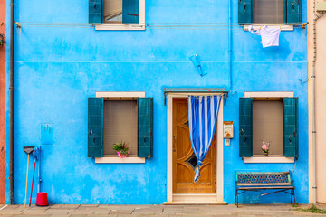 Blue aqua colored house with flowers and bench. Colorful houses in Burano island near Venice, Italy. Venice postcard. Famous place for european tourism and travel