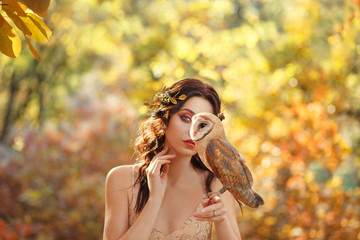 mysterious girl hides part of face behind owl sitting on the finger of a dark-haired attractive...