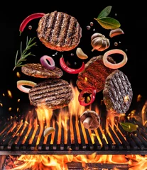 Photo sur Plexiglas Viande Beef milled meat on hamburger with vegetables and spices fly over the flaming grill barbecue fire.