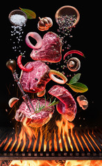 Raw beef steaks with vegetables and spices fly over the blazing grill barbecue fire.