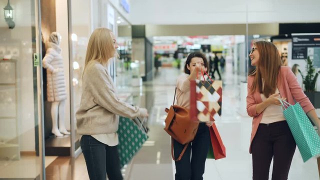 Pretty girls friends are having fun in shopping mall dancing and turning around with paper bags, smiling and laughing enjoying purchases and free time.
