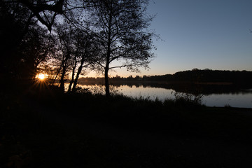 Sun just about to rise over lake - orange; trees to the left