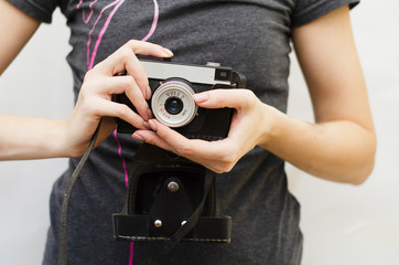a girl in a gray t-shirt holding an old camera in her hands on a light background