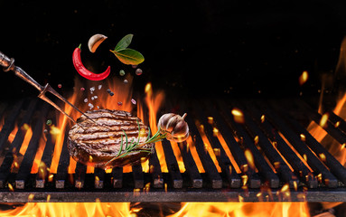 Beefsteak with spices fly over the flaming grill barbecue fire. - obrazy, fototapety, plakaty