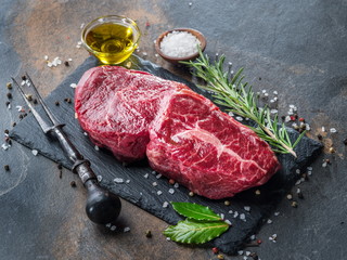 Raw  Rib eye steak or beef steak on the graphite board with herbs and spices.