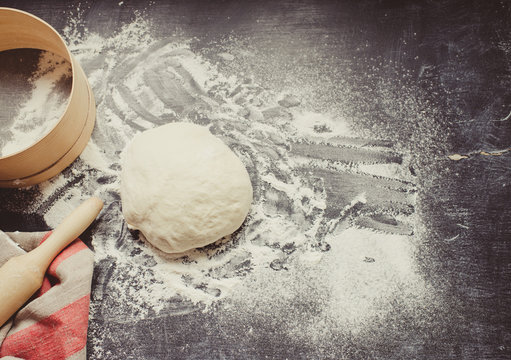 Baking background with dough and flour on dark table. 