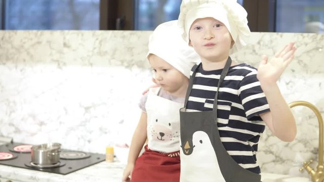 Brother and sister are photographed in the children's kitchen. Children look in different directions, the boy smiles, his younger sister is thoughtful