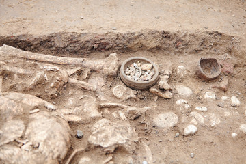 Archaeological excavations. Human remains (bones, skeleton and skull) in the ground, with little found artefacts in the tomb. Real digger process. Outdoors, copy space, close up.