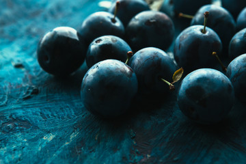 many fresh plums on blue background close up