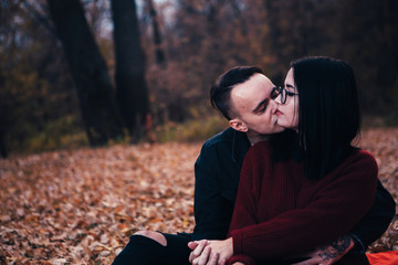 young man and young woman are sitting on a plaid in an autumn forest