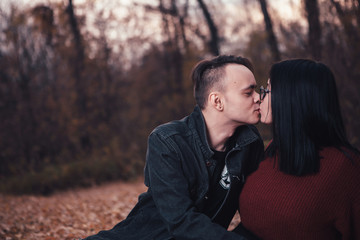 young man and young woman are sitting on a plaid in an autumn forest