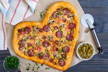 Tasty pizza in a heart shape with mushrooms, salami, pepperoni, olives, corn . The top view