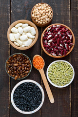 Healthy food, dieting, nutrition concept, vegan protein source. Assortment of colorful raw legumes: red lentils, green peas, beans, chickpeas in bowls, on a wooden table. Top view, flat lay background