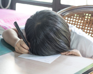 Asia kid girl doing boring homework with bored feeling at home. Female cute child concentrate write on paper. Asian students practice math subject for test. Student study at house