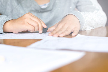 Close up kid's hand writing on paper, writing messy math on wooden table in room,student child girl holding pen doing homework at home, calculate the results on paper , education concept
