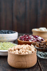 Healthy food, dieting, nutrition concept, vegan protein source. Assortment of colorful raw legumes: green peas, beans, chickpeas in bowls, on a wooden table.  Vertical view