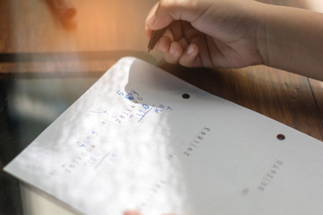 Close up kid's hand writing on paper, writing messy math on wooden table in room,student child girl holding pen doing homework at home, calculate the results on paper , education concept