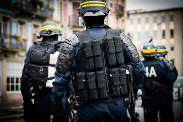 Rear view of police officers securing the zone in front of the Yellow vests movement protesters on Quai des Bateliers street detail on their guns, rifles, baton, gas tear guns, 