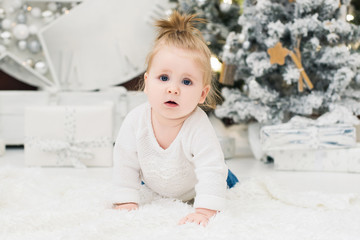 Baby girl on a background of Christmas trees, lights and gift boxes