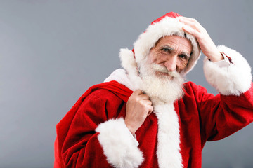 Santa Claus with a white beard wearing Santa outfit standing on the gray background and put his hand on his hat, New Year, Christmas, holidays, souvenirs, gifts, shopping, discounts, shops,