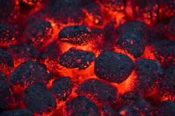 Coals smolder and glow. Residual flame from smoldering coals in cinder, closeup view. Flicker of...