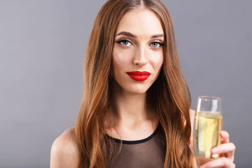Portrait of pretty long haired woman with red lips wearing black dress standing on the gray background while drinking champagne, New Year, Christmas, holidays, souvenirs, gifts, shopping, discounts
