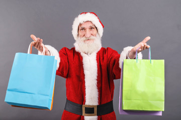 Santa Claus with a white beard wearing Santa outfit presents a lot of purchases on the gray background, New Year, Christmas, holidays, souvenirs, gifts, shopping, discounts, shops