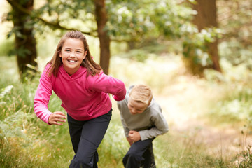 Fototapeta premium Two children walking in a forest amongst greenery smiling at camera, front view, focus on foreground