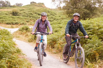 Naklejka premium Senior couple riding mountain bikes in a country lane during a camping holiday smiling, front view