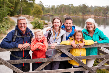 Multi generation family standing behind a wooden fence looking to camera, Lake District, UK