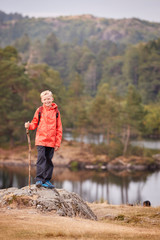 Naklejka premium A boy standing on a rock by a lake holding a stick, smiling to camera, Lake District, UK, vertical