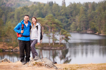 Young adult couple standing on a rock beside a lake in countryside, smiling to camera, full length