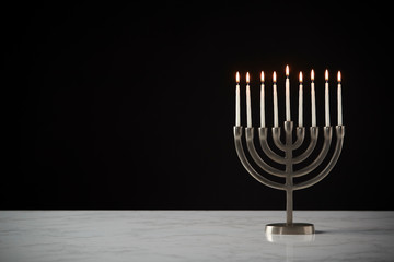 Lit Candles On Metal Hanukkah Menorah On Marble Surface Against Black Studio Background