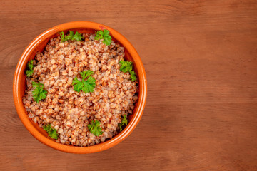 An overhead photo of cooked buckwheat in an earthenware bowl, garnished with fresh parsley leaves, on a dark rustic wooden background with a place for text