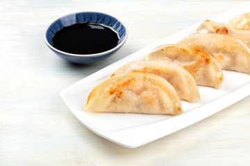 A closeup photo of gyozas, Asian dumplings, with soy sauce on a rustic wooden table with a place for text
