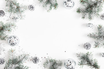 Christmas composition. Frame made of fir tree branches, silver decorations on white background....