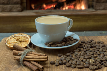 Cup of coffee with milk and coffee beans around the cup, cinnamon sticks, orange candied fruits.