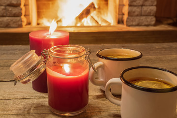 Cozy scene against fireplace with white enameled mugs with tea, and two candles.