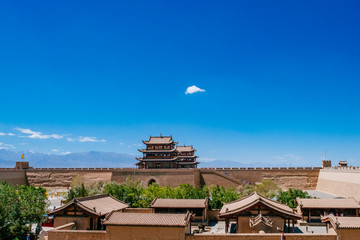 Gate tower building and city walls over local houses, under clear blue sky, at Jiayu Pass, in...