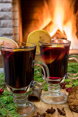Mulled wine glintwine in drinking glasses and christmas decorations, against cozy fireplace background.