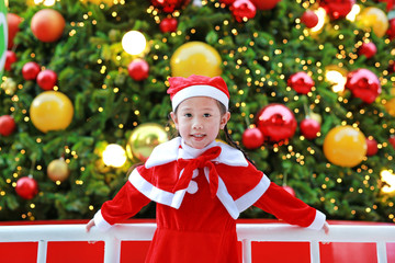 Smiling little kid girl in Santa costume with Christmas background. Merry Christmas and happy holidays.
