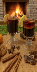 Mulled wine glintwine in drinking glasses and christmas decorations, against cozy fireplace background.