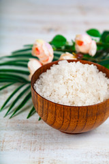 Wooden bowl with sea salt, rose and palm leaf.
