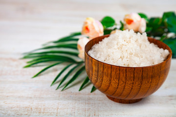 Fototapeta na wymiar Wooden bowl with sea salt, rose and palm leaf.