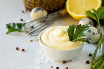 Homemade Mayonnaise Sauce in a white bowl on a light stone table. Copy space.