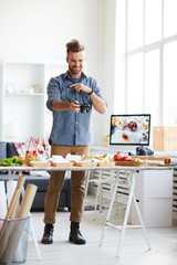 Full length portrait of smiling photographer taking pictures of party table with food in photo studio, copy space