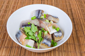 Slices of smoked Atlantic mackerel with greens in bowl closeup